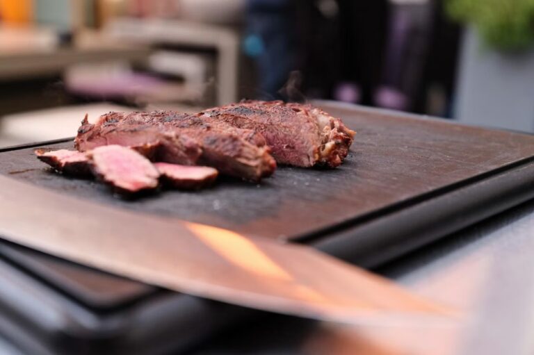 Ein Steak liegt auf einem Schwarzen Brett neben einem Messer beim Kochkurs