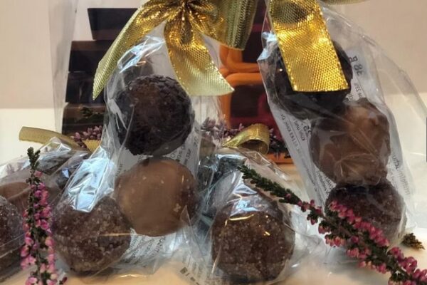 Man sieht handgemachte Pralinen in einer Plastikverpackung mit goldener Schleife.