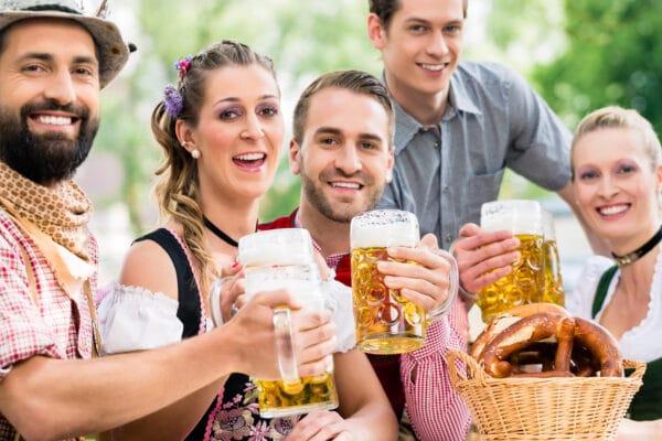 Fünf Personen in traditioneller bayrischer Tracht stoßen mit Bier gefüllten Maßkrügen bei der Oktoberfest-Olympiade an