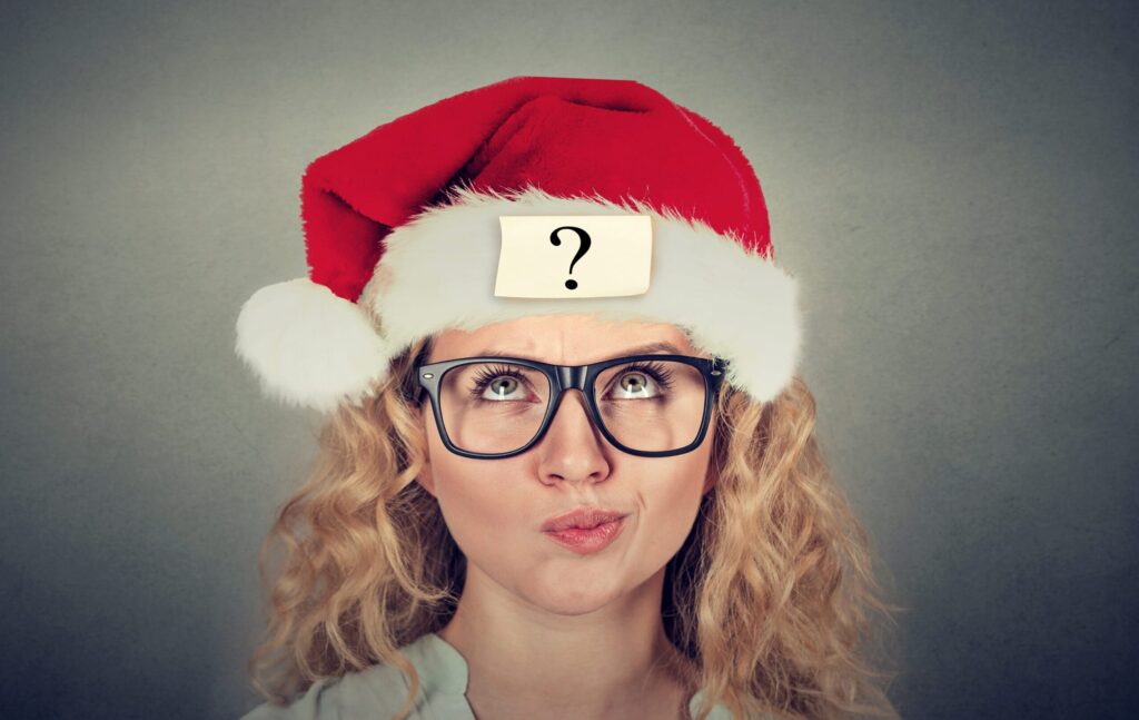 Eine blonde Frau mit Brille und Weihnachtsmütze schaut fragend nach oben bei dem Event Weihnachtliches Team-Quiz