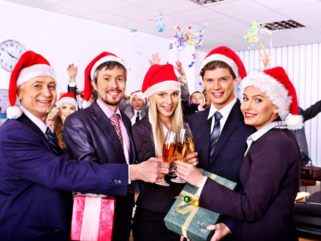 Vier Personen Business-Look, tragen Weihnachtsmützen und stoßen mit Sektgläser an .